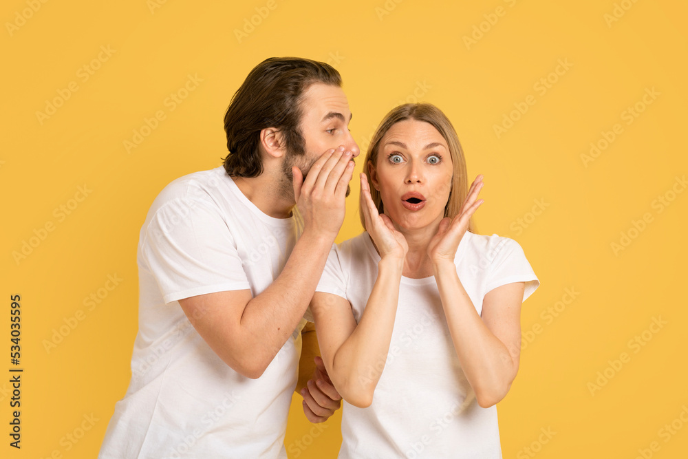 Cheerful young caucasian guy whispering into ear of shocked woman in white t-shirt Cheerful young caucasian guy whispering into ear of shocked woman in white t-shirt