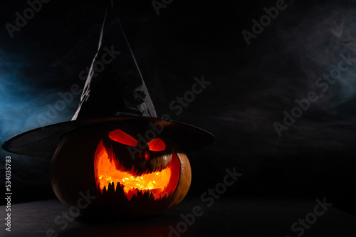 A creepy pumpkin with a carved grimace in the smoke. Jack o lantern in the dark.