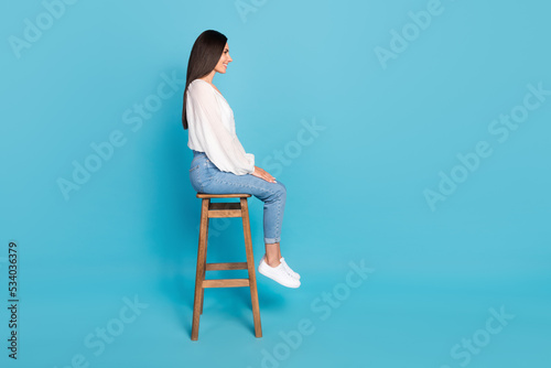 Full length profile portrait of adorable cheerful person sit chair look empty space isolated on blue color background