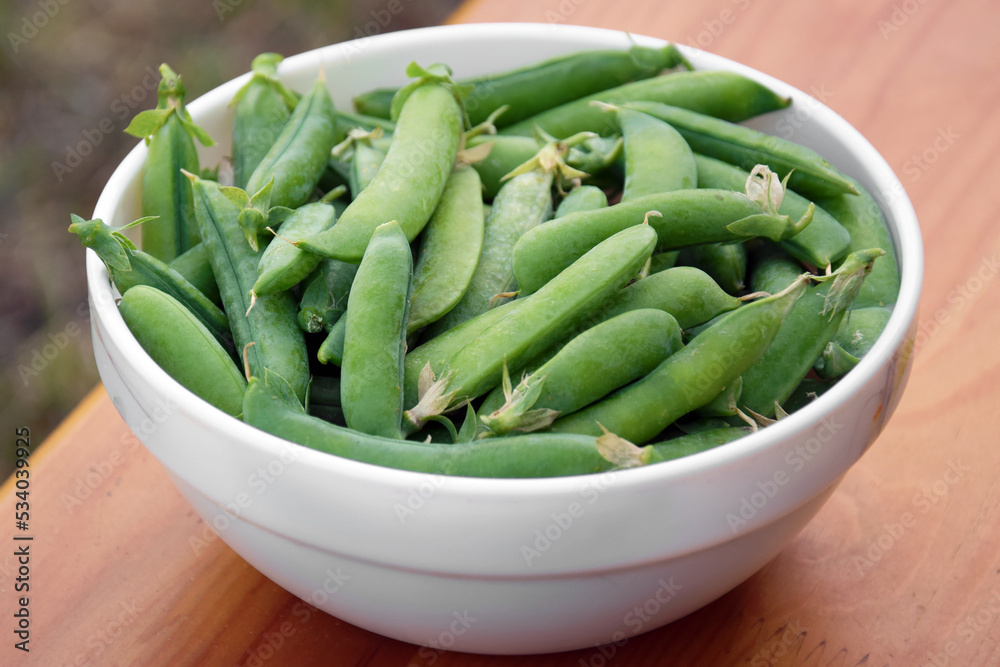 Green peas in a white plate on a wooden bench. Green peas in a white plate on a wooden bench.