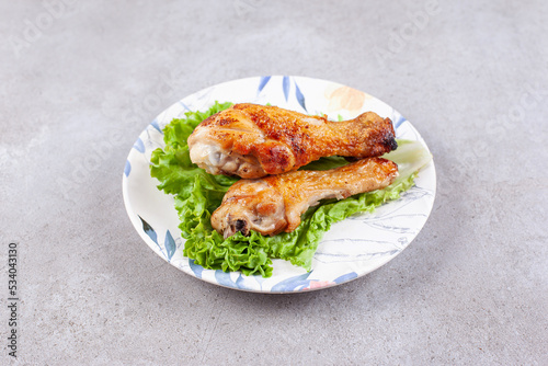 Grilled chicken legs meat with lettuce on white plate