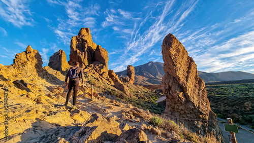 Man with backpack hiking with scenic golden hour sunrise morning view on unique rock formation Roque Cinchado, Roques de Garcia, Tenerife, Canary Island, Spain, Europe. Pico del Teide volcano summit photo