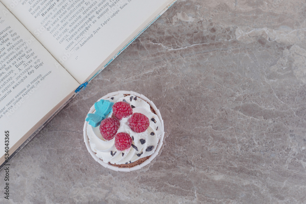 A cupcake and an open book on marble background A cupcake and an open book on marble background