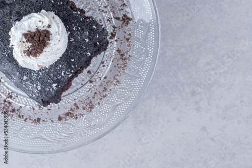 Small slice of chocolate cake on a glass platter on marble background