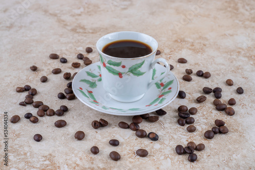 Scattered coffee beans around a cup of coffee on marble background