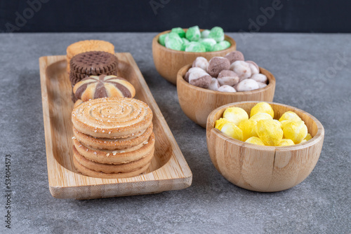 Bowls of candies and a small tray with cookies on marble background