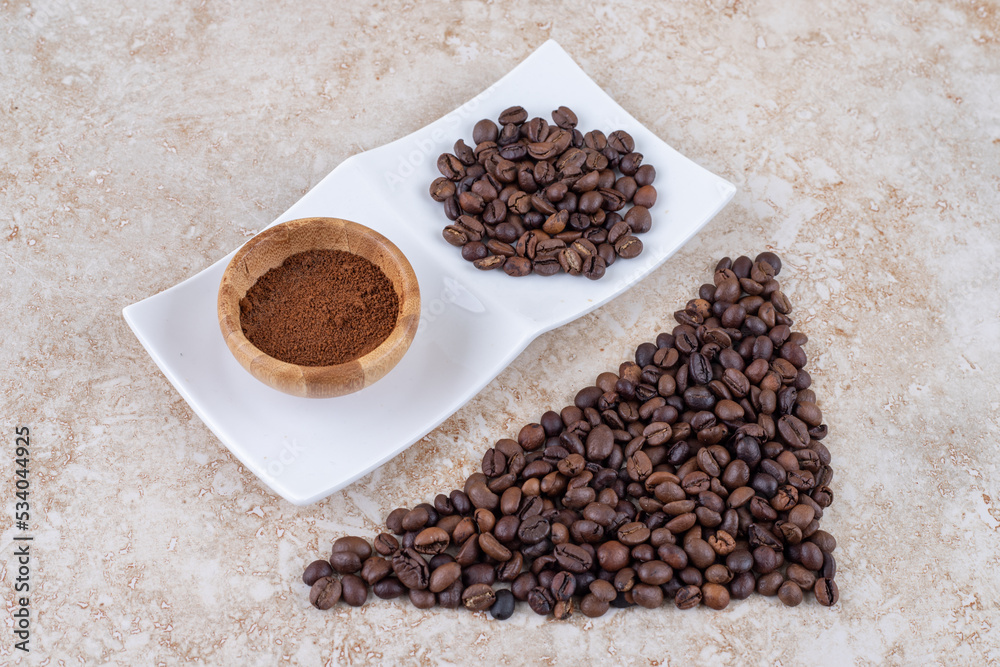 Coffee bean piles and a small bowl of ground coffee on marble background Coffee bean piles and a small bowl of ground coffee on marble background