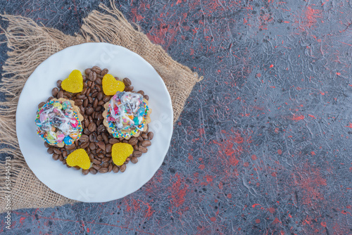 Fototapeta Naklejka Na Ścianę i Meble -  Coffee beans, marmalades and cupcakes on a platter on abstract background