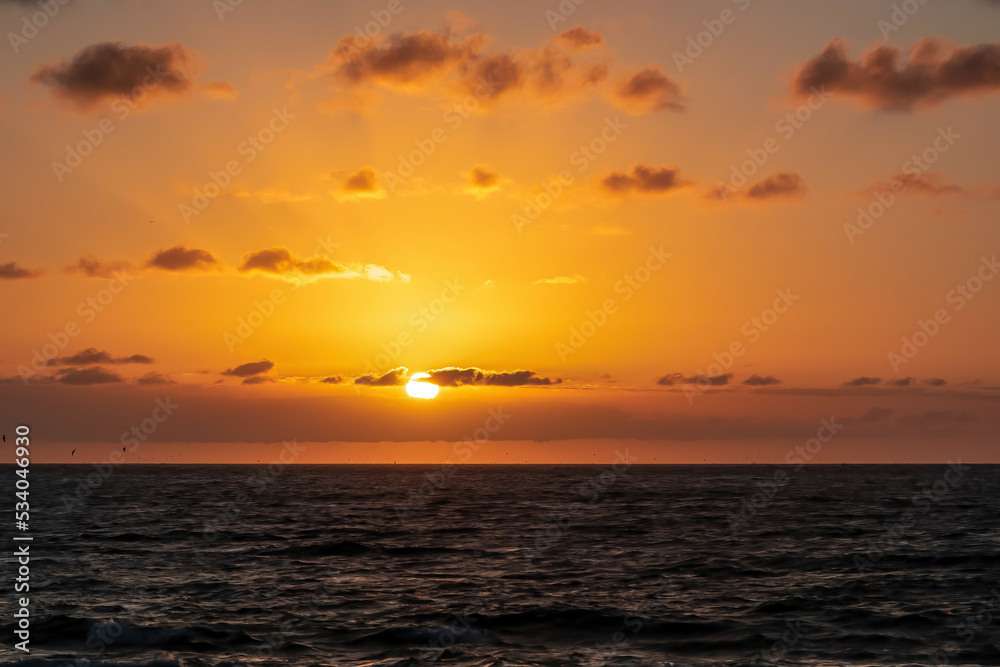 Scenic view during sunset from the beach Playa del Ingles in Valle Gran Rey, La Gomera, Canary Islands, Spain, Europe. Clouds emerging and turning orange red. Sun is going down behind the horizon