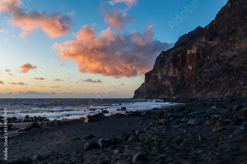 Scenic view during sunset on the volcanic sand beach Playa del Ingles in Valle Gran Rey  La Gomera  Canary Islands  Spain  Europe. Massive cliffs of the La Mercia range. Calm atmosphere at the seaside