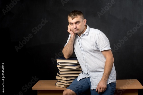 a man of European appearance sits on a table near a stack of books. student thought