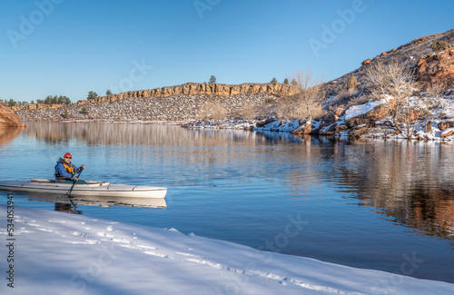 senior male wearing life jacket is paddling expedition canoe in winter scenery of Horsetooth Reservoir in northern Colorado photo