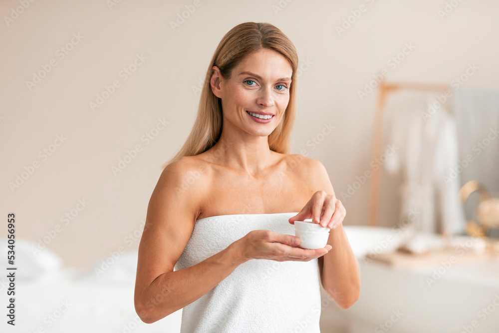 Skincare cosmetics. Happy middle aged woman trying new moisturising cream, making beauty routine at home Skincare cosmetics. Happy middle aged woman trying new moisturising cream, making beauty routine at home