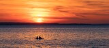 Panoramic shot of the sea with the silhouettes of two people in a boat at orange sunset