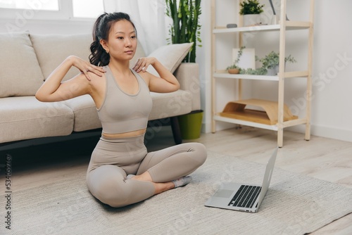 Young Asian woman in front of her laptop sports and yoga repeating exercises on the video at home in lotus position stretching the muscles of the neck, a set of home workouts for the body lifestyle