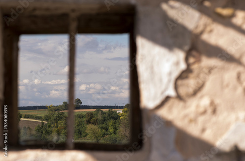 Pola i drzewa , niebo i chmury , widziane , jak obraz w ramie , poprzez okienko starego , zniszczonego  domu .