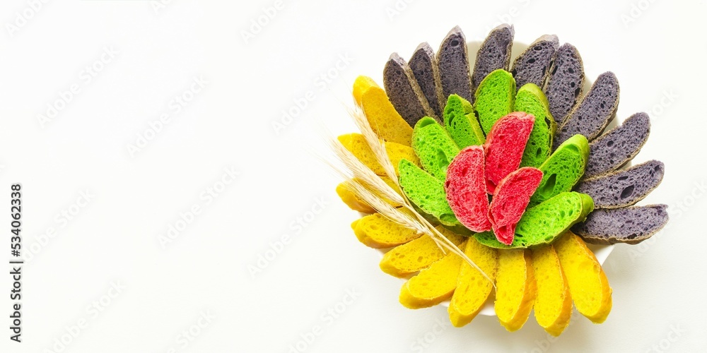 On a white background is a large white plate with colored sliced bread. Adding colors makes the bread more stylish, beautiful, amazing. Banner, copy space for text. Concept amazing food. On a white background is a large white plate with colored sliced bread. Adding colors makes the bread more stylish, beautiful, amazing. Banner, copy space for text. Concept amazing food.