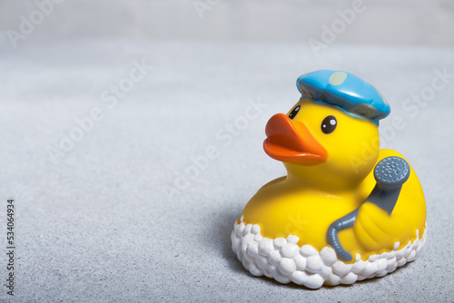 Yellow rubber duck for a bath in a bath cap and with a shower head in the wing on a light background