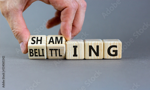 Shaming and belittling symbol. Concept words Shaming and Belittling on wooden cubes. Businessman hand. Beautiful grey table grey background. Business shaming and belittling concept. Copy space.