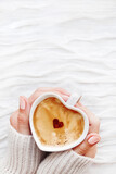 Top view on womans hand with cup of hot coffee with cinnamon heart. Winter and Valentine's Day cozy background. Copy space on fabric backdrop.