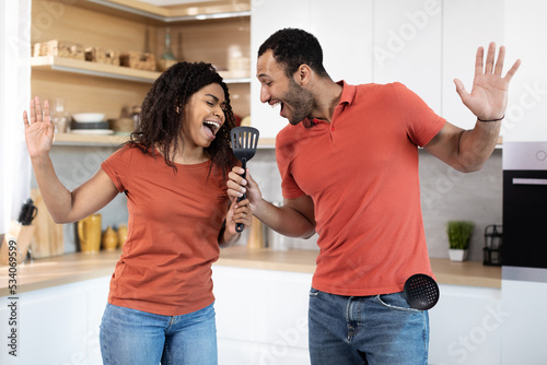Satisfied millennial african american lady and man have fun, dance together, enjoy music, sing at imaginary microphone