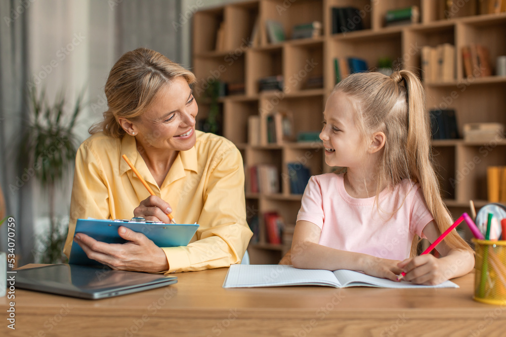 Preparation for preschool. Clever girl drawing at specialist cabinet, woman psychologist watching her and making notes Preparation for preschool. Clever girl drawing at specialist cabinet, woman psychologist watching her and making notes