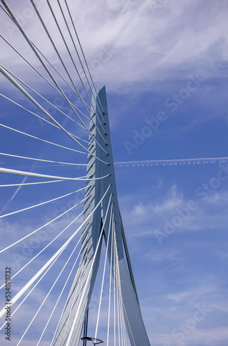Rotterdam, Netherlands - July 11, 2022: Erasmusbrug, bridge. Fisheye closeup of the Swan's. neck with the cables, all white construction against blue cloudscape