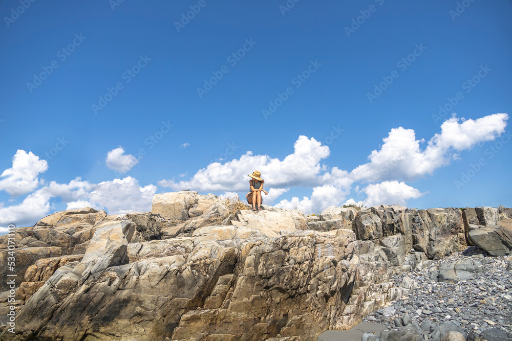 Woman sitting on the rocks in front of the ocean with clouds in the sky