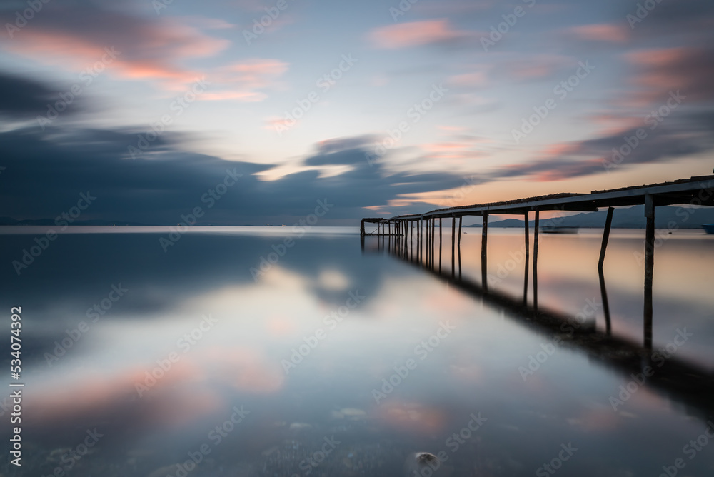 Long exposure photography, wodden pier on foreground and silky sea water and colorful clouds on horizon as a background