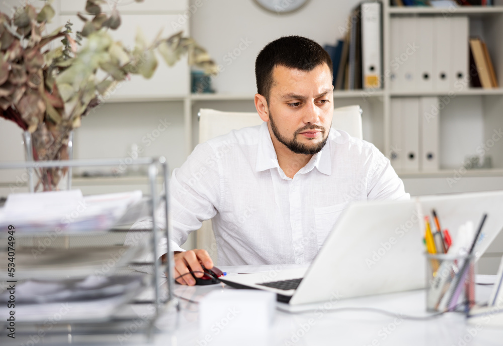 Fototapeta premium Man office worker sitting at desk and using laptop during his workday.