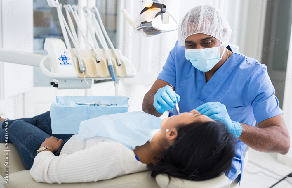 Obraz premium Professional african american dentist performing teeth treatment to adult woman in dental clinic