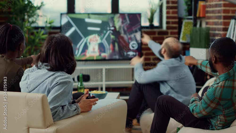 Diverse people playing video games to have fun at home, enjoying online shooting challenge on television console. Using controller to play competition at social gathering with friends. Diverse people playing video games to have fun at home, enjoying online shooting challenge on television console. Using controller to play competition at social gathering with friends.