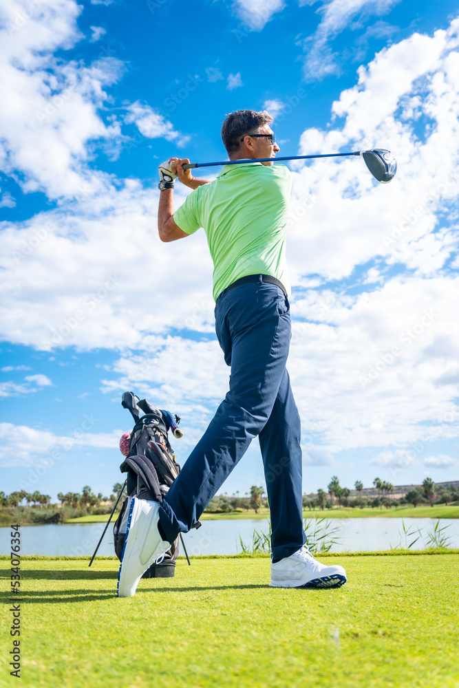 Obraz premium A player playing golf on the golf course, hitting the ball next to a lake, vertical photo