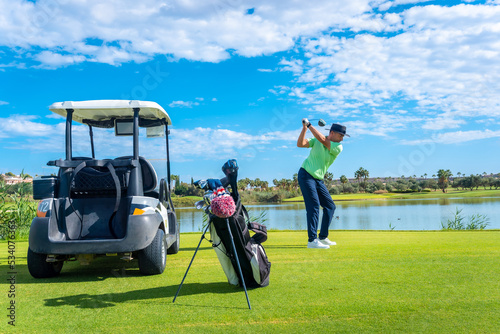 Man playing golf at golf club by a lake, hitting the ball next to the buggy car