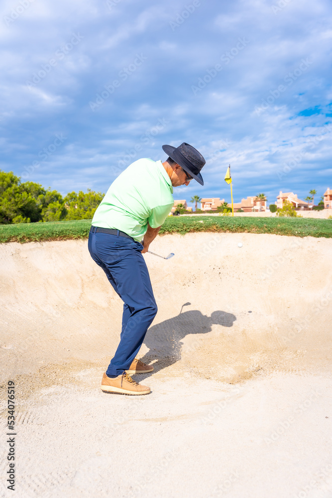 Man playing golf, getting the ball out of the bunker by hitting the ball with the pitching wedge stick Man playing golf, getting the ball out of the bunker by hitting the ball with the pitching wedge stick