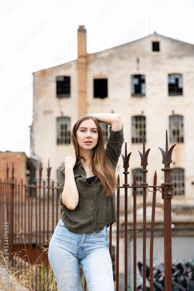Street style photo of elegant fashionable woman wearing trendy clothes. Model walking in street near wrought-iron fence