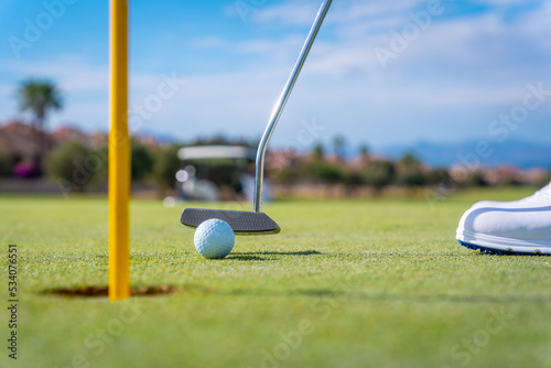 Detail of a man playing golf, putting the ball into the hole on the green with the putter
