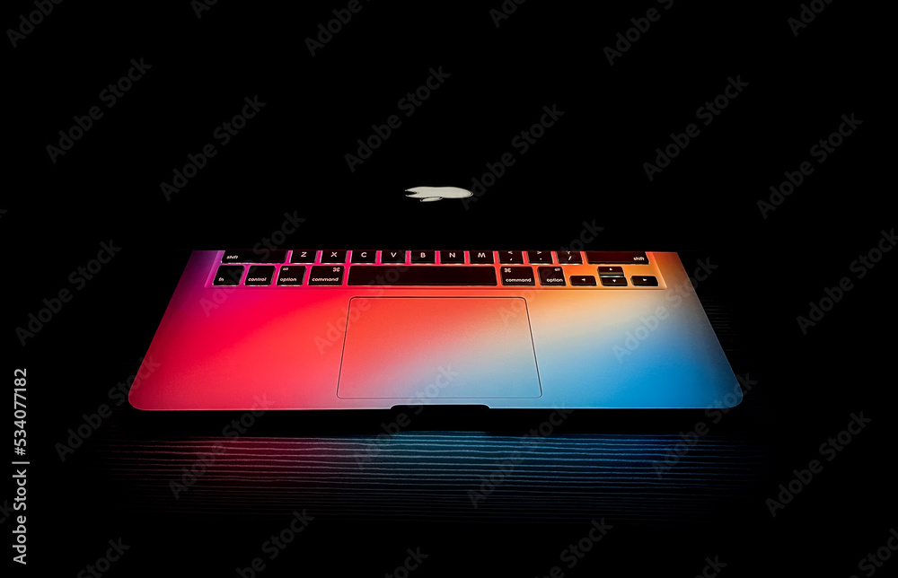 Apple macbook Laptop with backlit logo, half lid open on a table lit