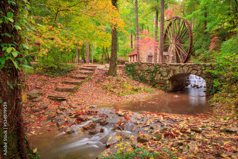 Autumn scene of stone building with water mill wheel  with stone steps leading to silky effect stream through rocks