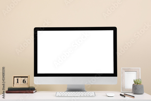 Comfortable workplace with blank computer display on desk near beige wall. Space for text