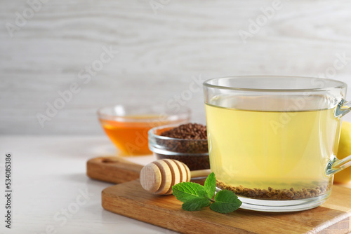 Cup of aromatic buckwheat tea, mint, honey and granules on white table, space for text photo