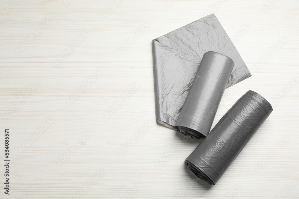 Fototapeta premium Rolls of grey garbage bags on white wooden table, flat lay. Space for text