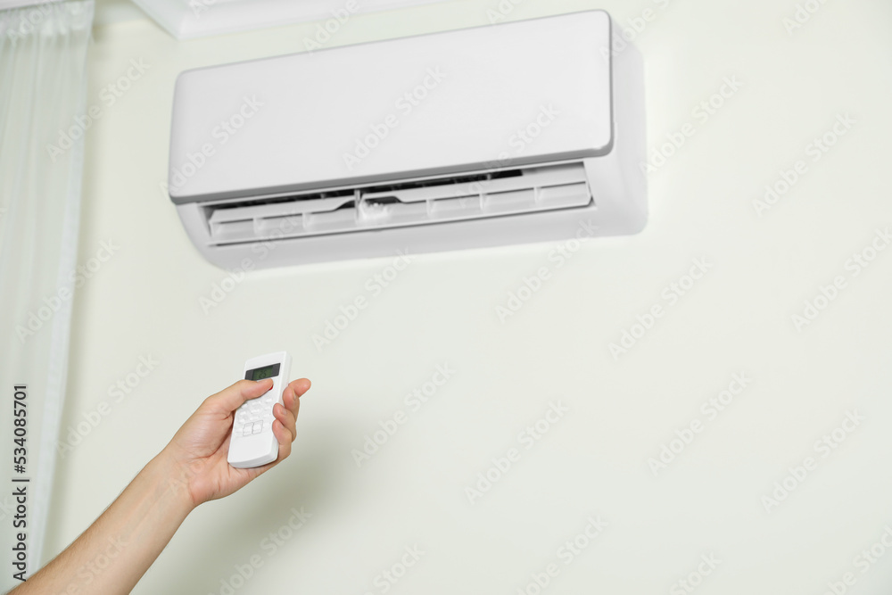 Fototapeta premium Man operating air conditioner with remote control indoors, closeup