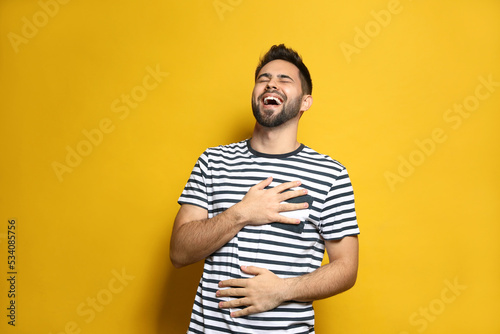 Young man laughing on yellow background. Funny joke