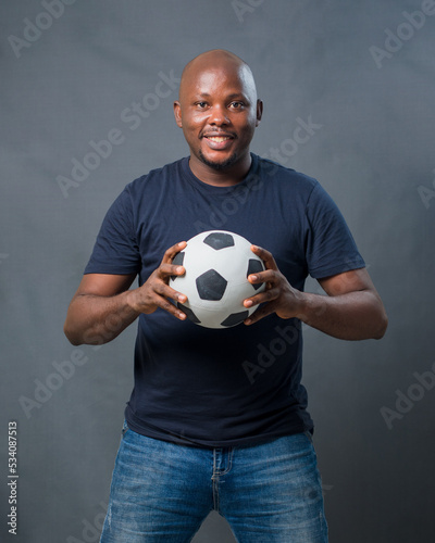 An excited African man or guy holding a black and white football in his hands while looking at the camera