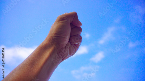 Male fist isolated on blue sky background. Asian clenched hand, gesturing up. Counting, aggression, brave, masculinity concept
