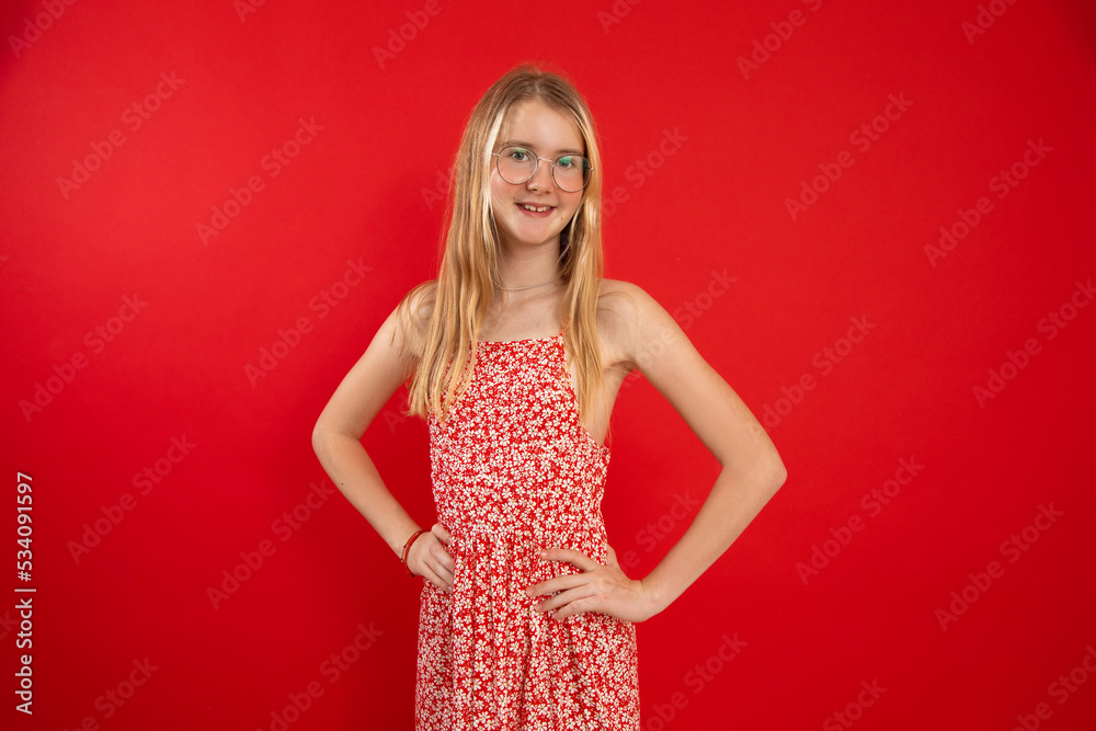Portrait of smiling beauteous teenage girl with fair hair wearing light summer dress, glasses, holding hands on waist. Portrait of smiling beauteous teenage girl with fair hair wearing light summer dress, glasses, holding hands on waist.