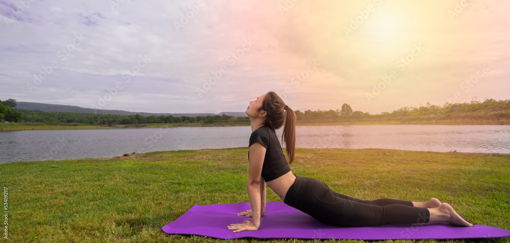Fototapeta premium Portrait of a beautiful woman practicing yoga outdoors. beautiful girl practicing cobra asana in class calm and relax woman's happiness horizontal blurred background