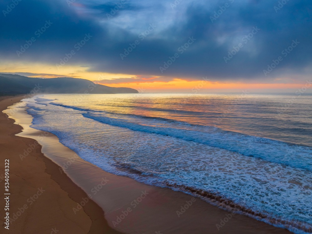 Fototapeta premium Peaceful sunrise over the ocean with small waves and clouds