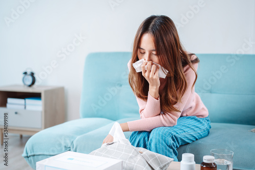 Asian young woman patient cold sick she sneeze with tissue paper on sofa, Female health problem blowing nose use pharmacy first aid box delivery service hospital, self recover health care concept.
